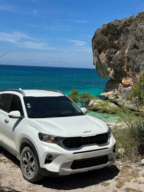 White Kia SUV from Vroom.do parked above a rocky turquoise cove on the Dominican coast