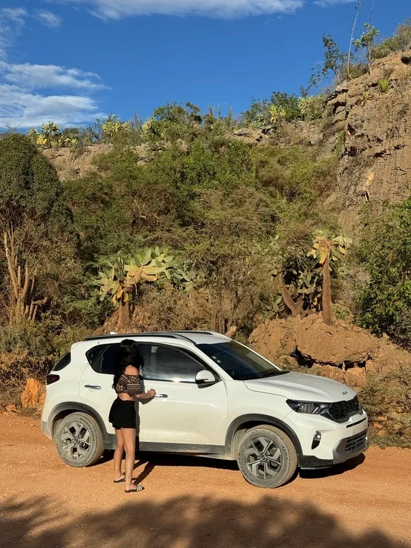 Traveller stepping out of a white rental SUV parked at a rocky viewpoint